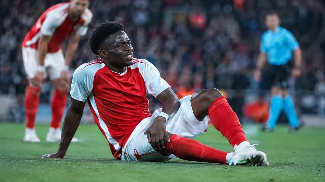 Bukayo Saka sitter på gresset og holder seg til låret under en fotballkamp.