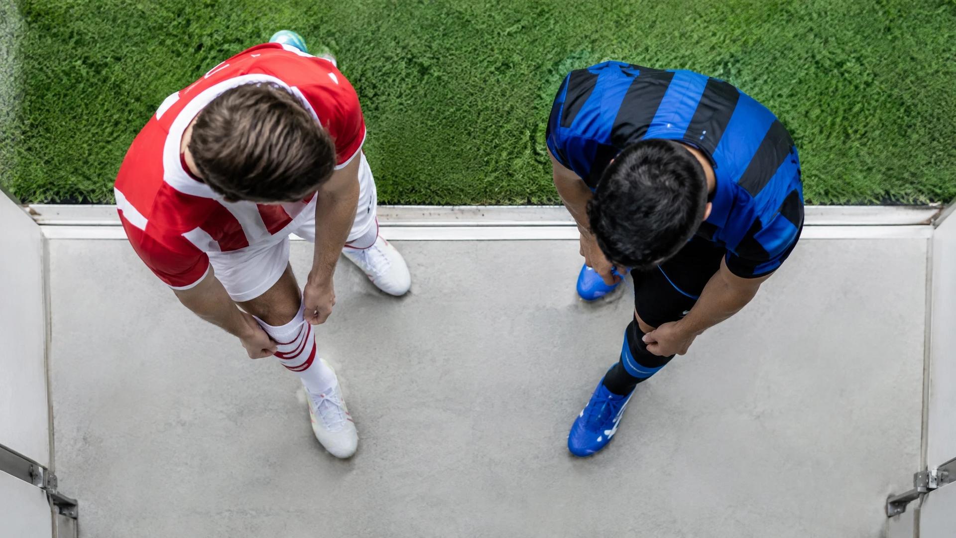 To fotballspillere i nøytrale drakter gjør seg klare ved spillertunnelen, sett ovenfra.