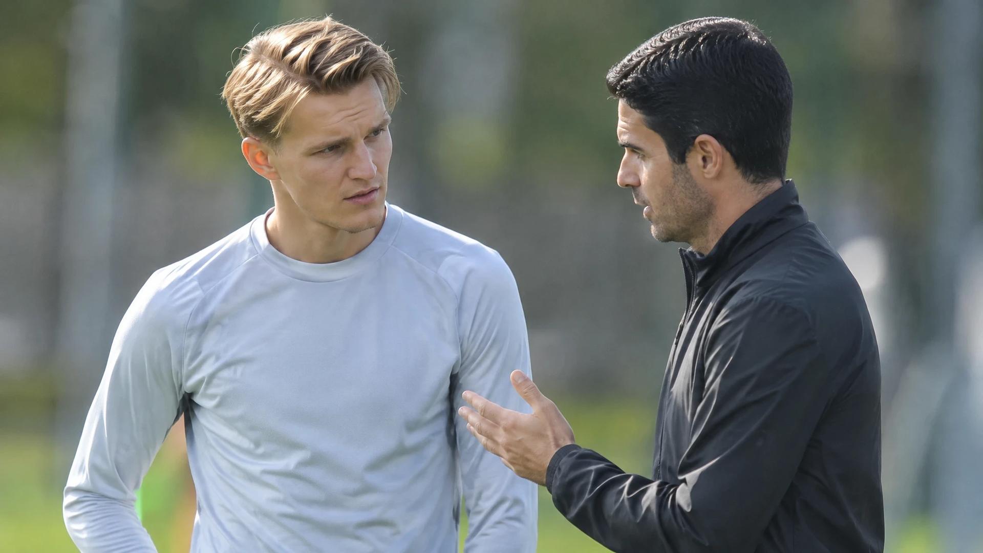 Martin Ødegaard og Mikel Arteta snakker sammen på en fotballtreningsbane.