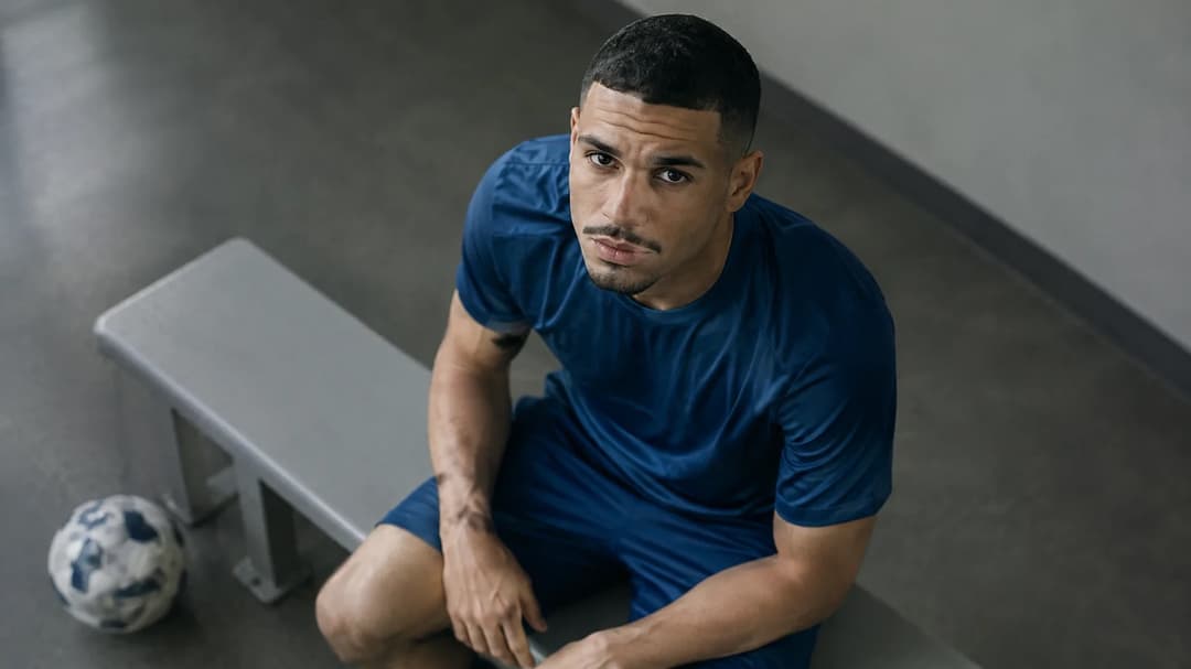 Maxence Lacroix sitter alene på en benk i et stille fotballmiljø.