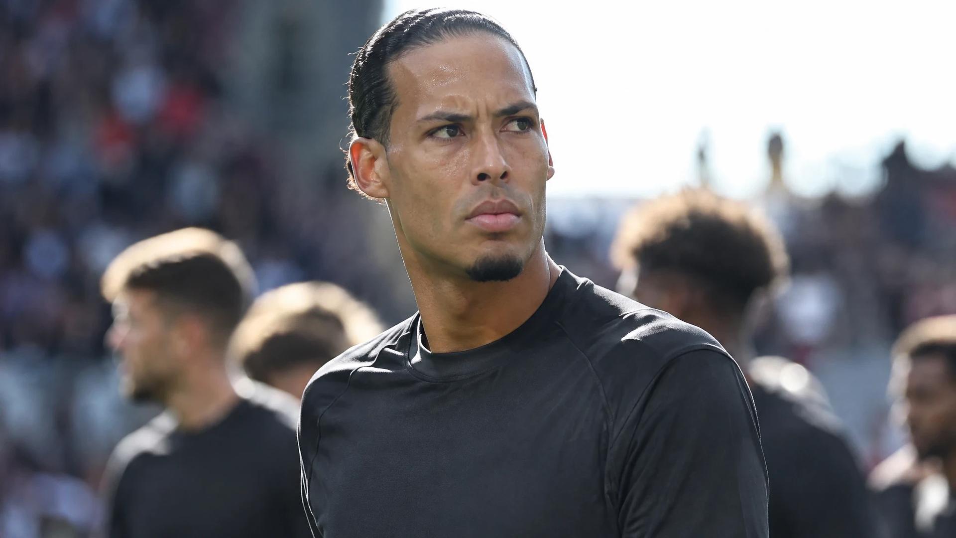 Virgil van Dijk står konsentrert i forgrunnen, med spillere og tilskuere ute av fokus i bakgrunnen.