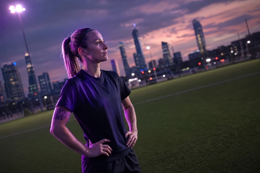 Esther González stands thoughtfully on the training pitch of Gotham FC, with the skyline of New Jersey in the background at dusk.