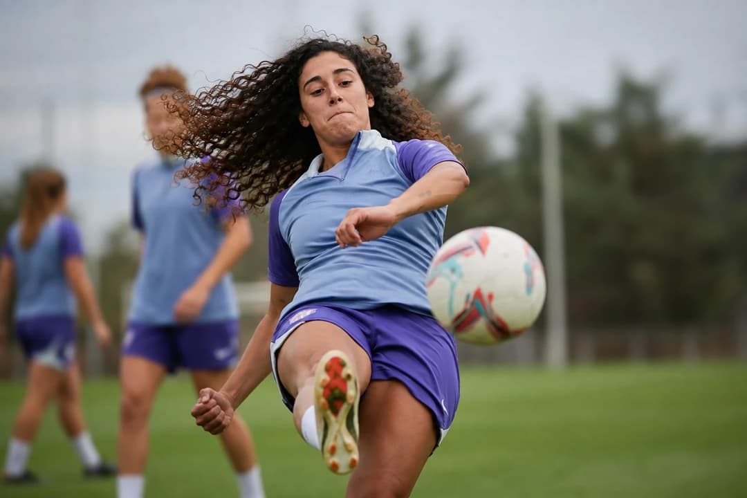 Celia Segura training at Atlético Madrid, striking a ball on a green training pitch.