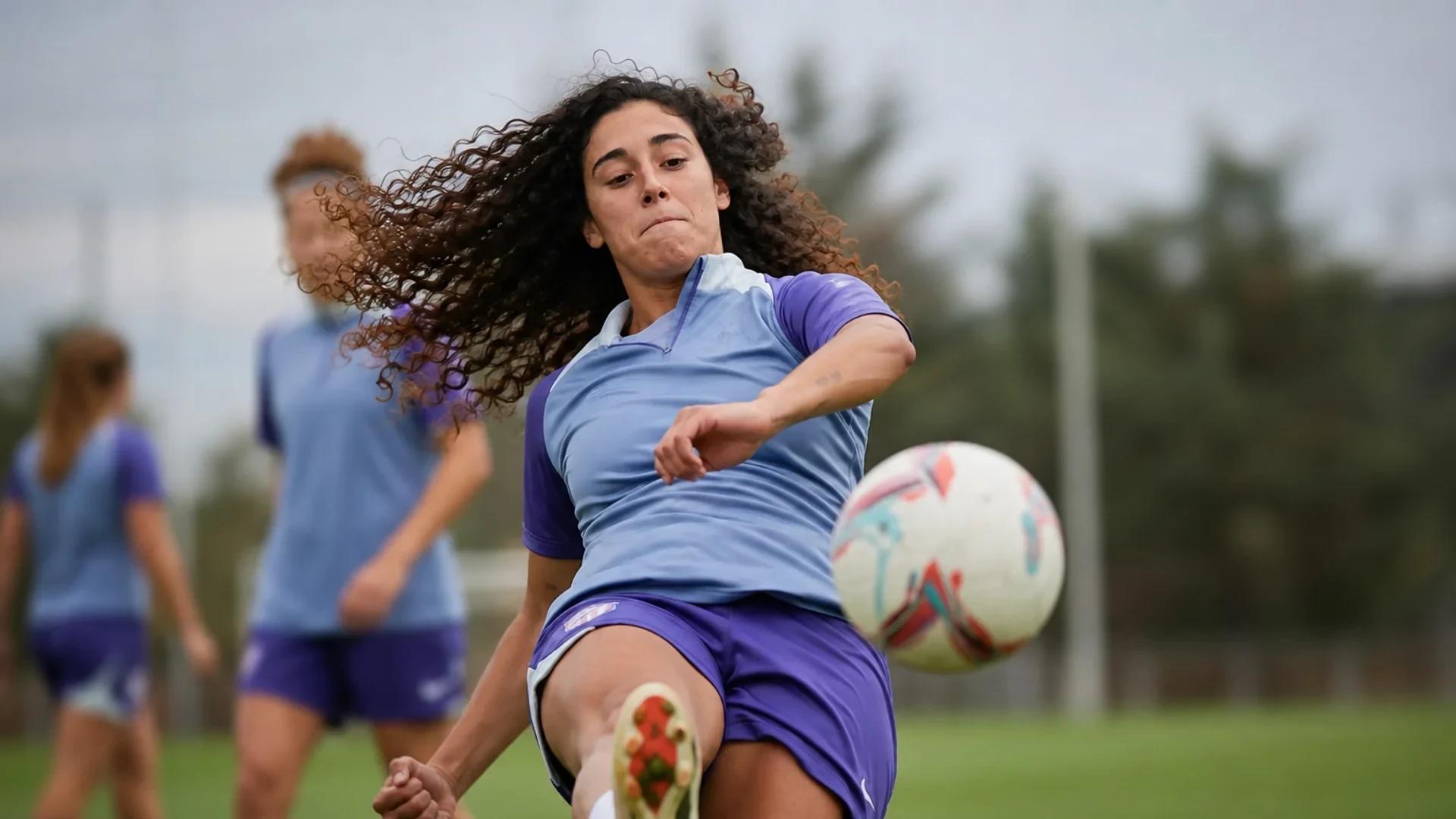 Celia Segura training at Atlético Madrid, striking a ball on a green training pitch.