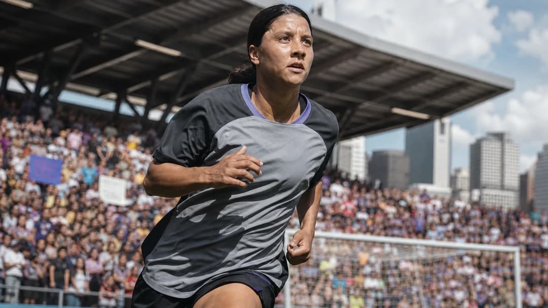 A female soccer player in motion during a game, with a vibrant stadium crowd in the background.