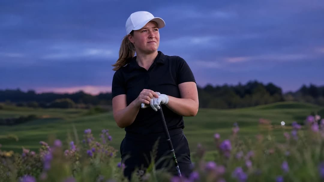 A woman golfer adjusting her club at dusk on a golf course with wildflowers in the foreground.