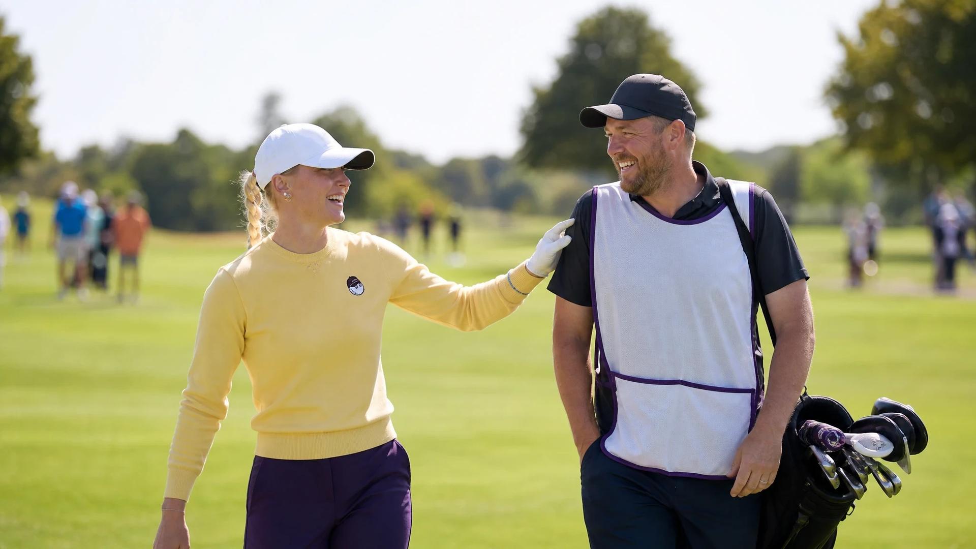 Charley Hull and caddie Adam Woodward share a lighthearted moment on a sunny golf course.