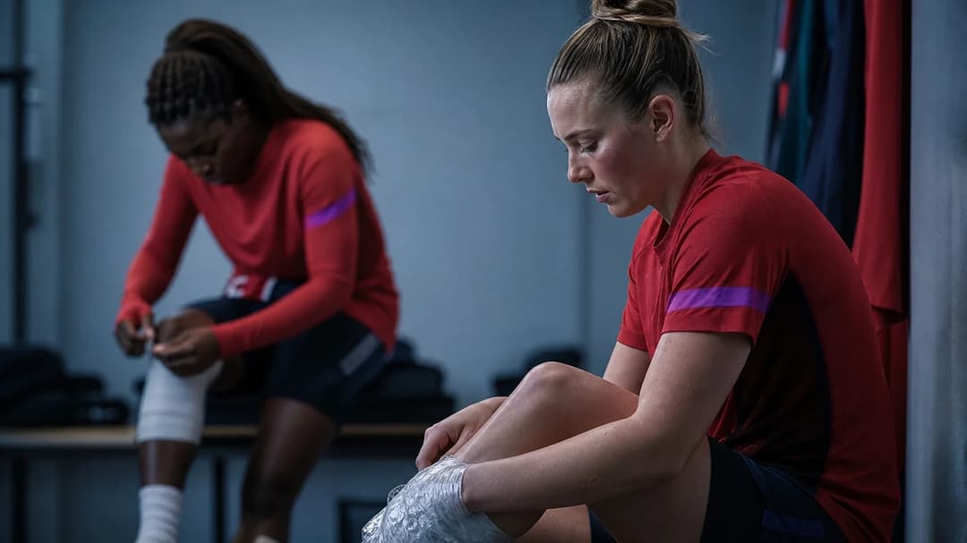 A close-up of two football players in a training room setting, one with an injured ankle, showcasing a moment of reflection.