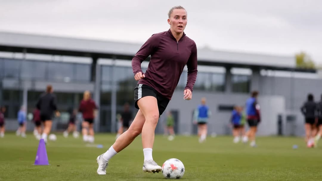 Laura Freigang dribbling a football on a training pitch, with teammates in the blurred background.