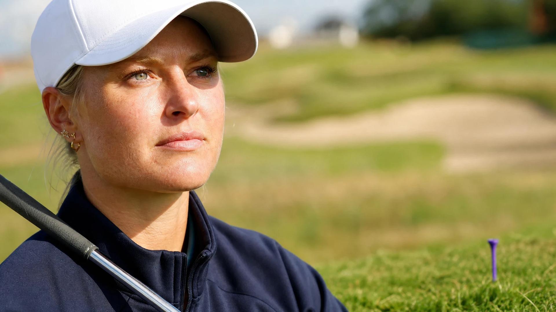 Anna Nordqvist on a golf course, deep in thought with a golf club resting on her shoulder.