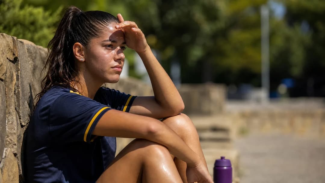 Iara Lobo sitting on a stone wall, wiping her brow after practice with a violet water bottle beside her.