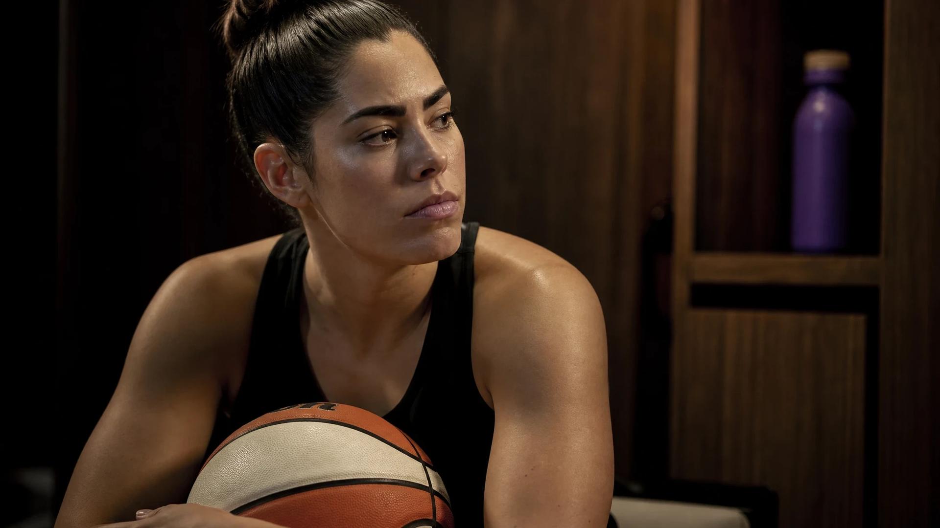 Kelsey Plum sitting in a locker room holding a basketball, looking contemplative.