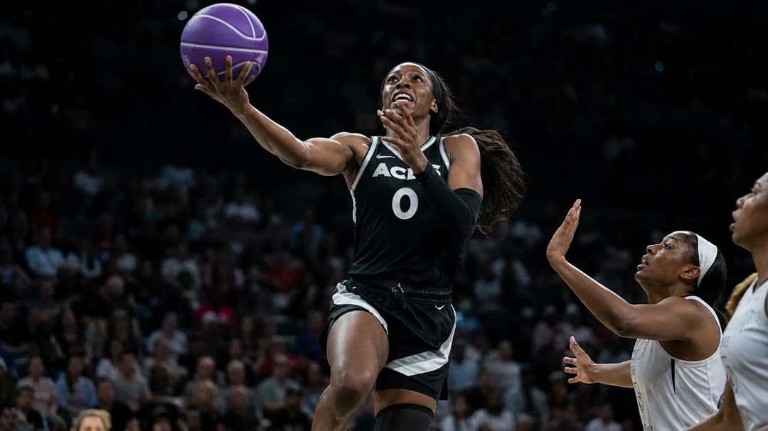 A female basketball player mid-air performing a layup during a game.