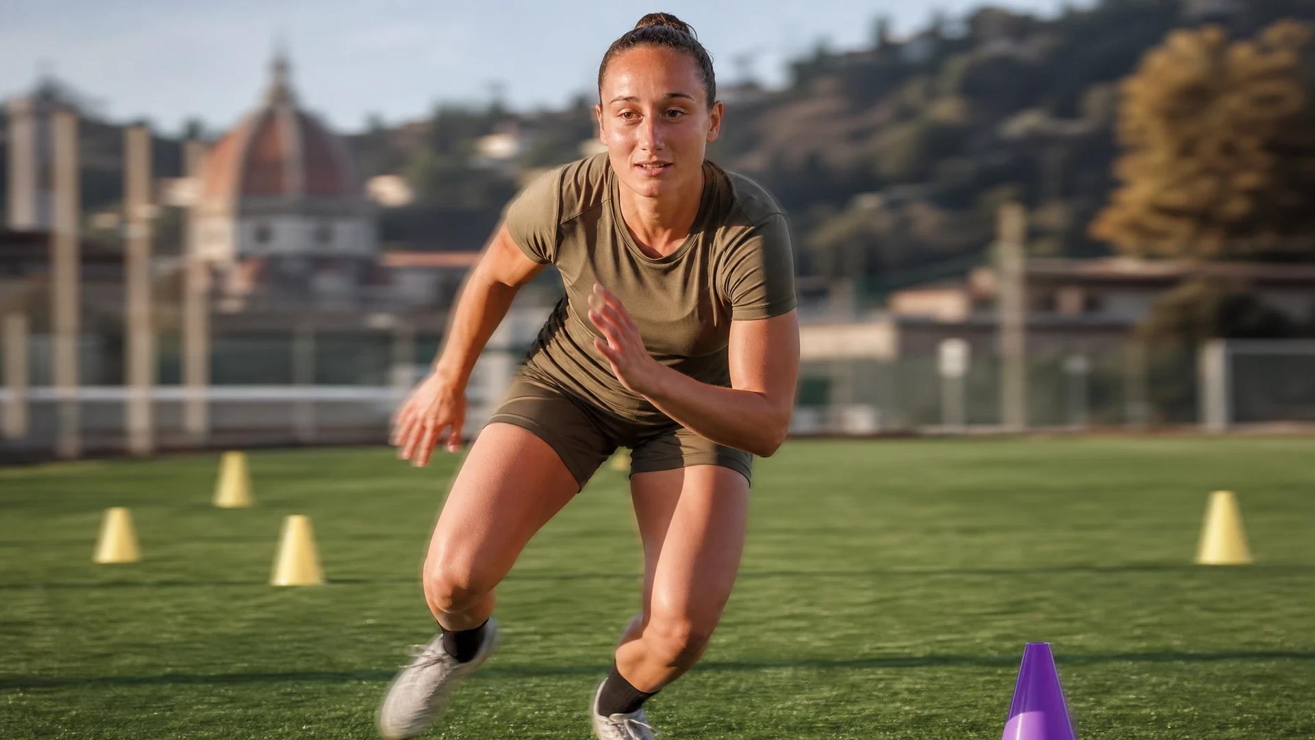 A young female footballer in motion during training, with a violet training cone visible in the scene.