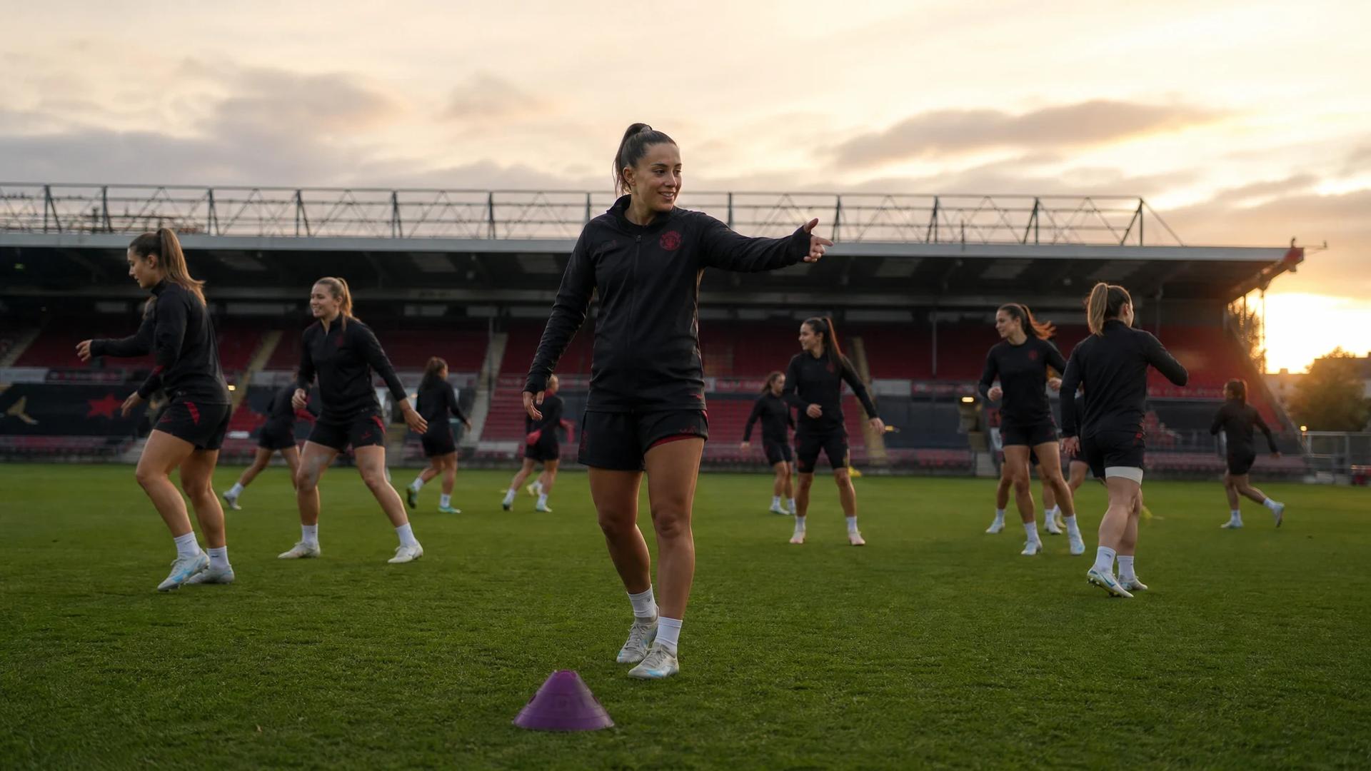 A training session of the Manchester United Women’s team at Old Trafford, with players in motion and a violet training cone on the pitch.
