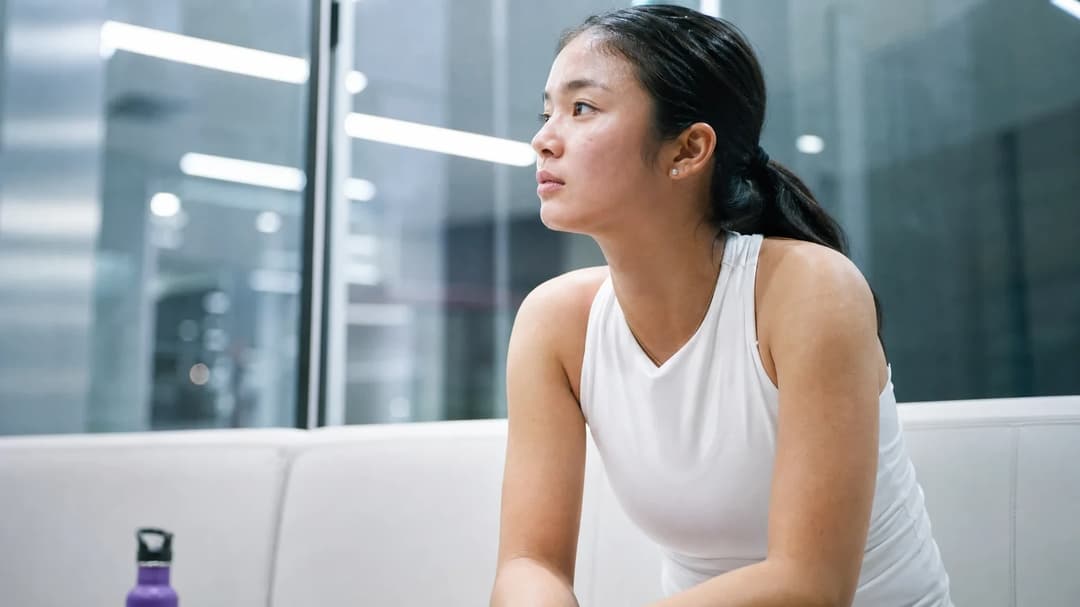 A young female tennis player reflecting on her victory in a clubhouse, with a violet water bottle next to her.