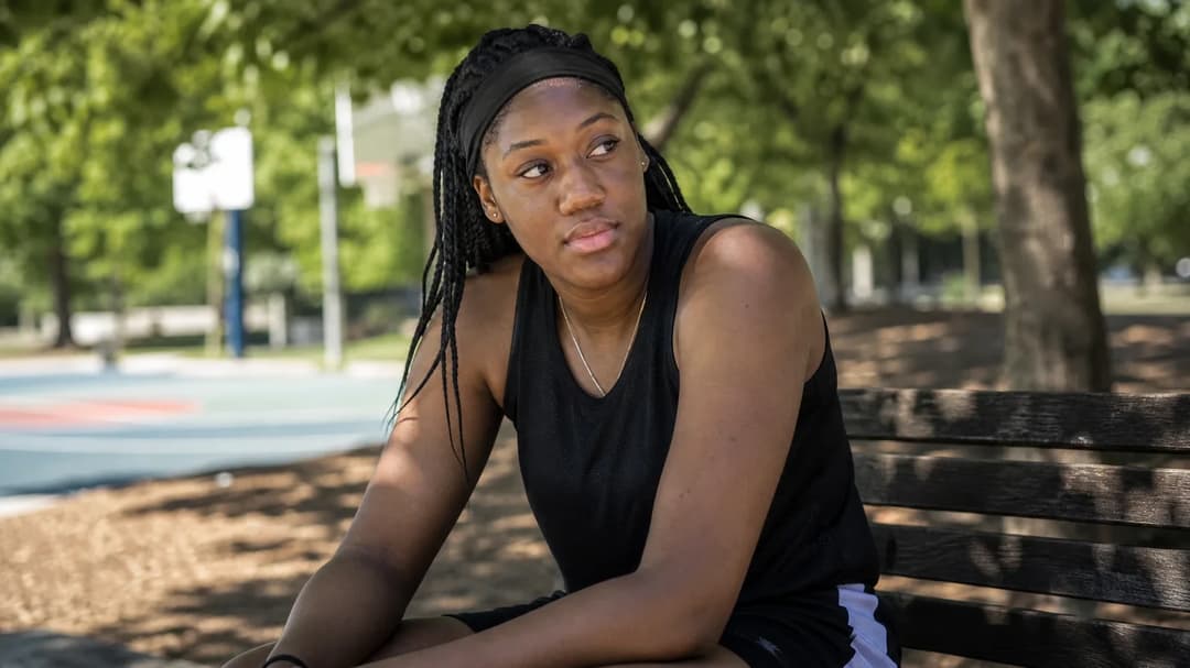 A portrait of Shakira Austin sitting on a bench, looking thoughtful in a park-like setting.