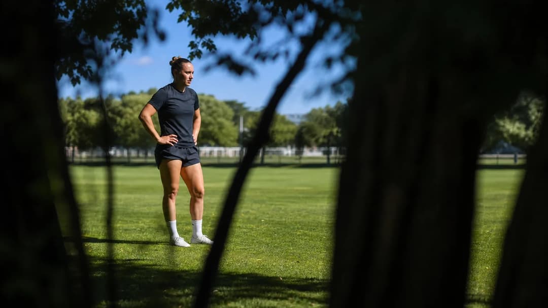 Christin Meyer stands contemplatively at the training ground, partially framed by shadows from nearby trees.
