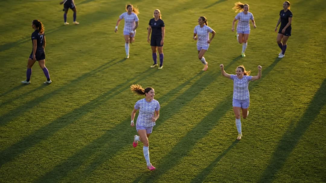 Aerial view of two players celebrating a goal on a football field during sunset.
