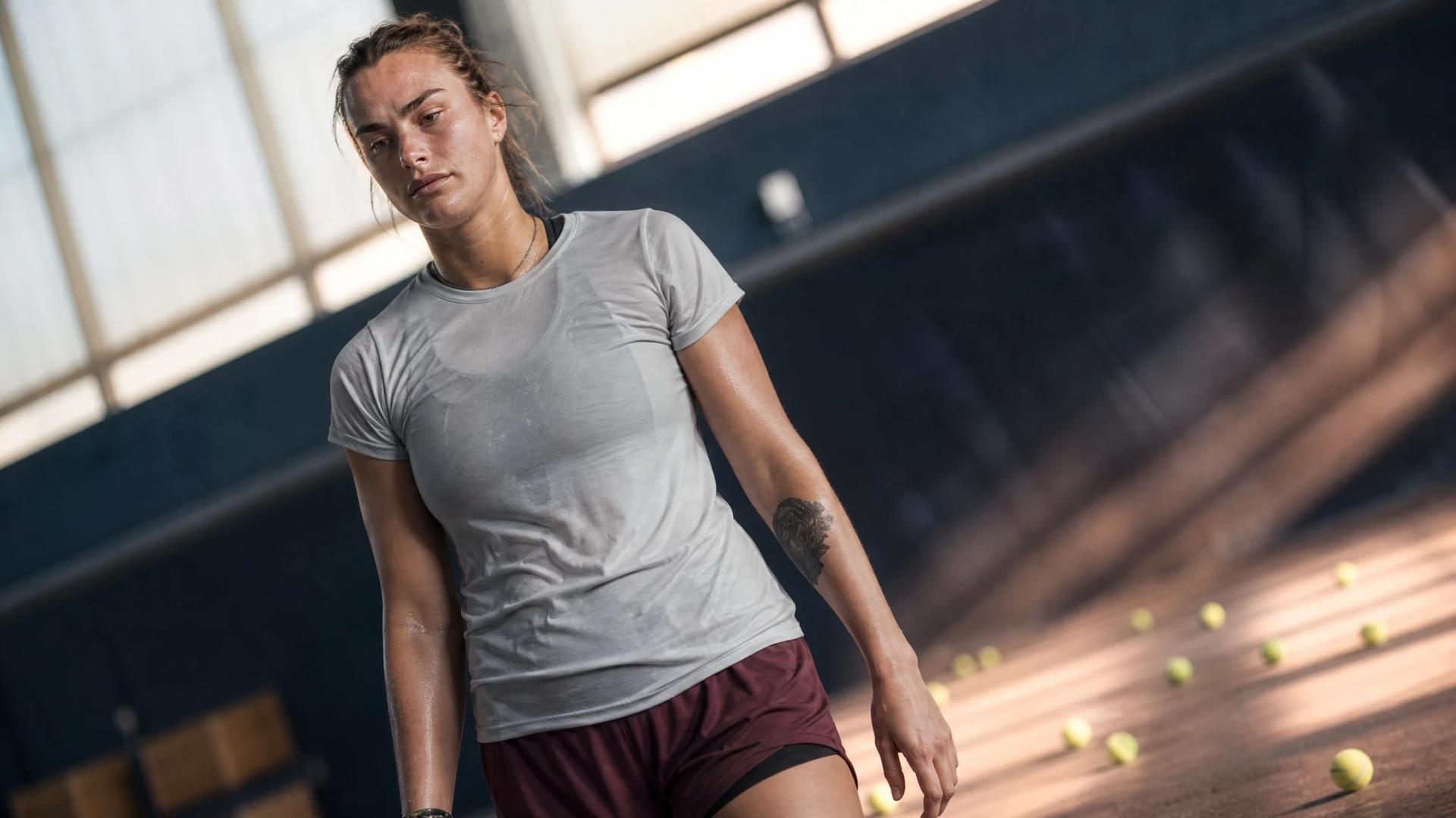 A reflective Aryna Sabalenka stands on a tennis court after her defeat, with a low-angle view capturing her expression.