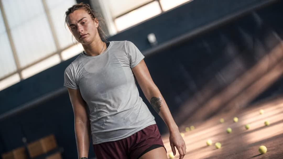 A reflective Aryna Sabalenka stands on a tennis court after her defeat, with a low-angle view capturing her expression.