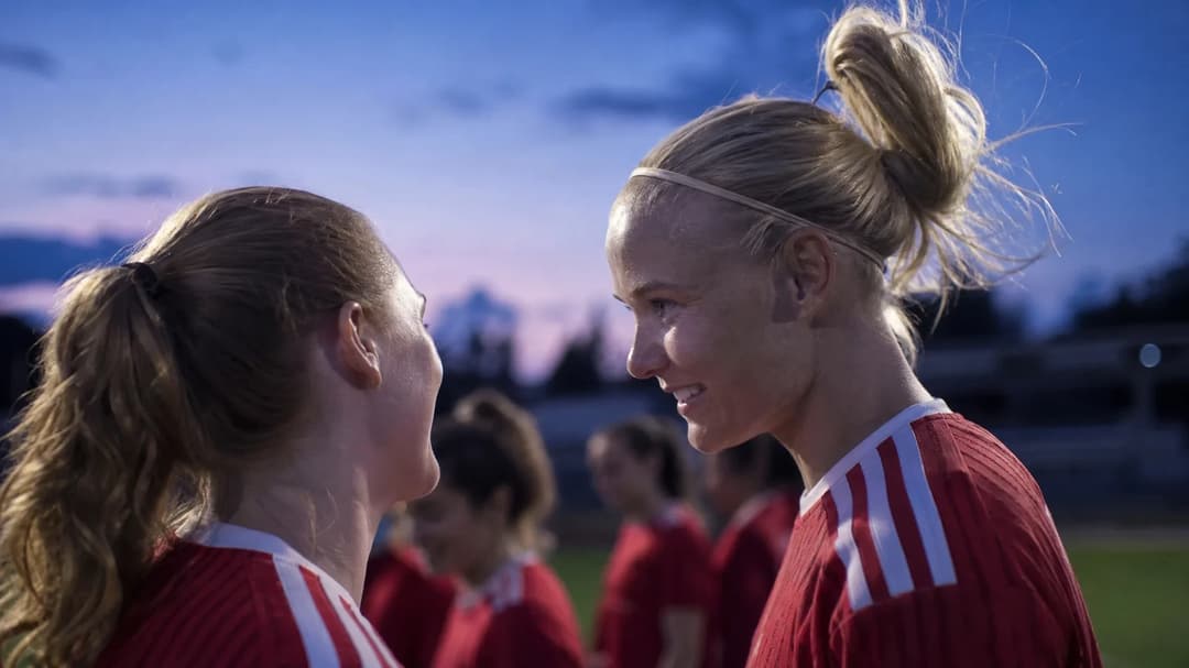 Close-up of two female football players in a dusk setting, showing their expressions of anticipation before a match.