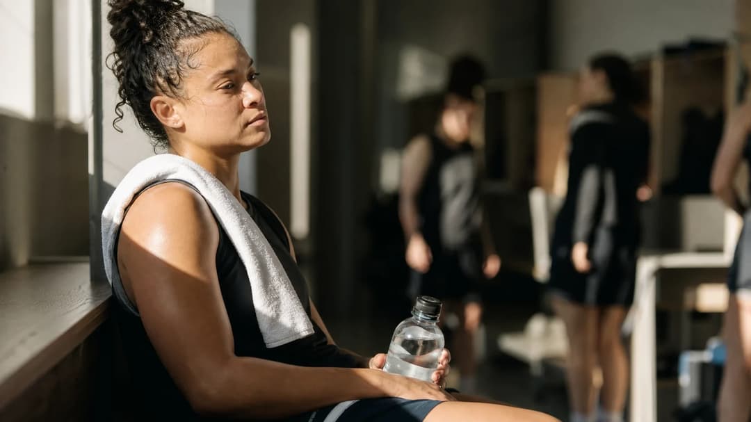 A female basketball player reflecting quietly in a locker room, illuminated by sunlight.