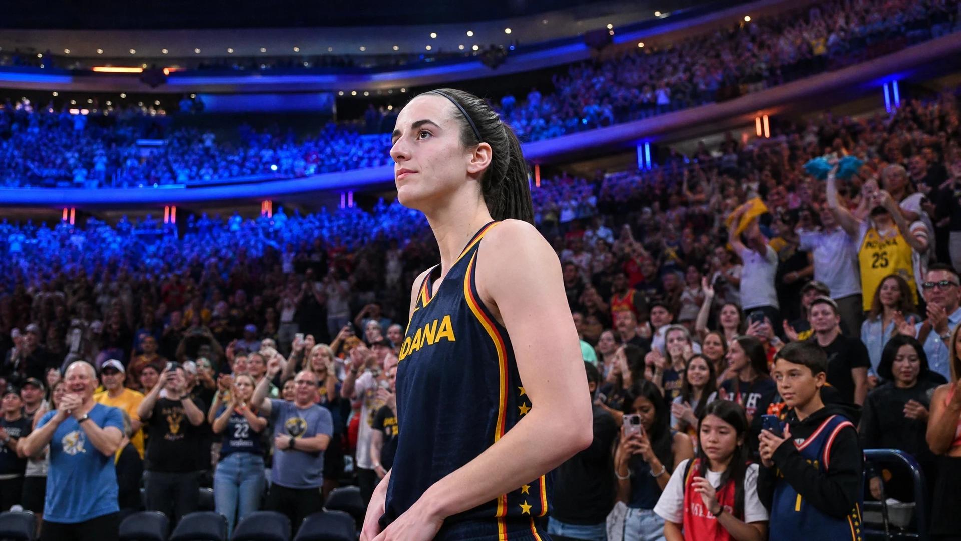 Caitlin Clark standing in a basketball court surrounded by cheering fans, illuminated by colorful lights.