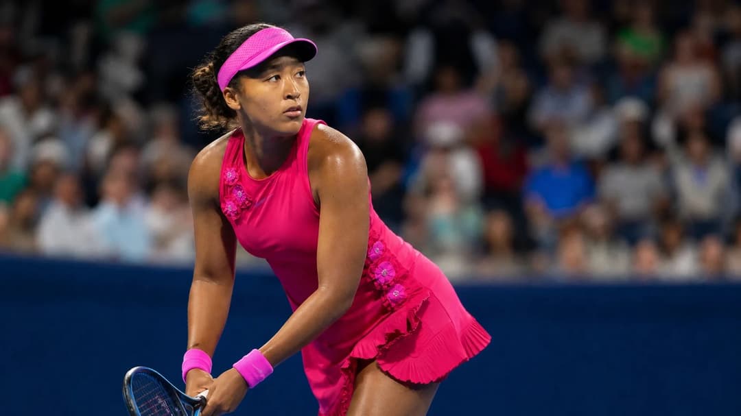 Naomi Osaka in a poised stance on the tennis court, captured in a moment of anticipation.