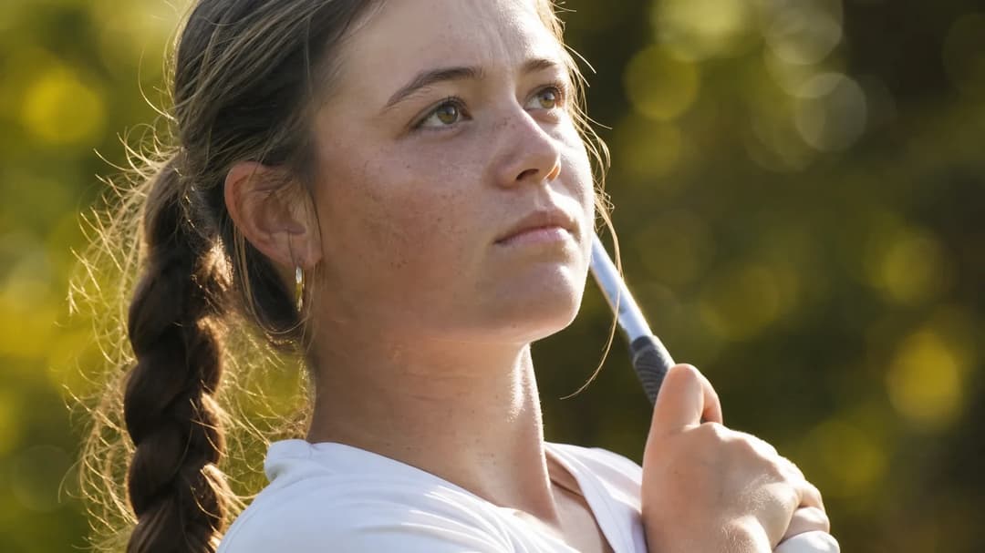 A close-up of a young female golfer preparing with focused determination.