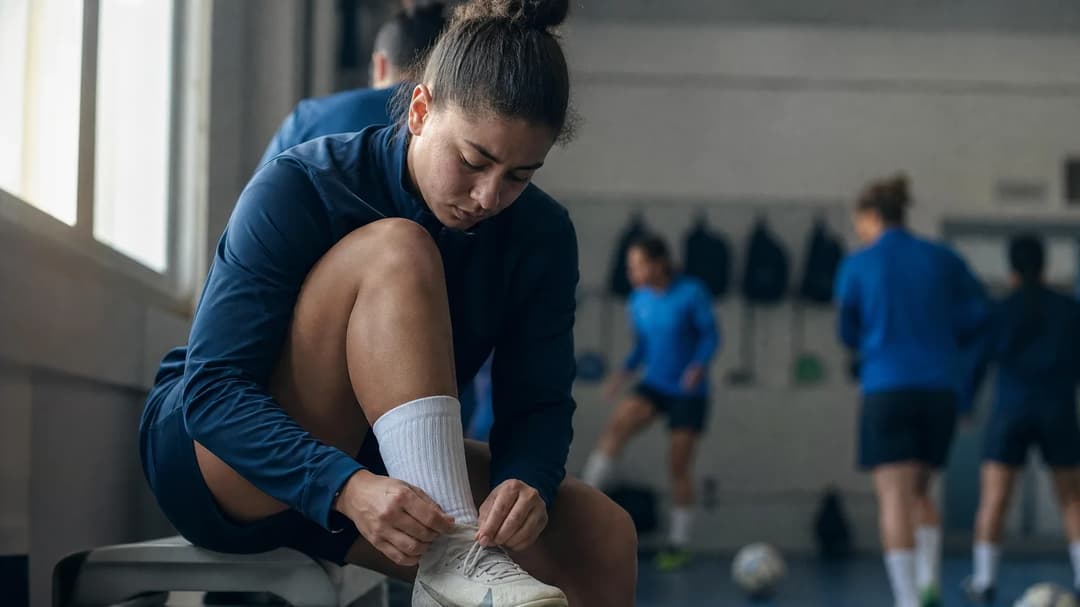 A close-up of Carla Camacho preparing her football boots in a training room.