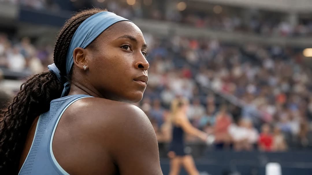 Coco Gauff watches from the sidelines as a match unfolds in the background.