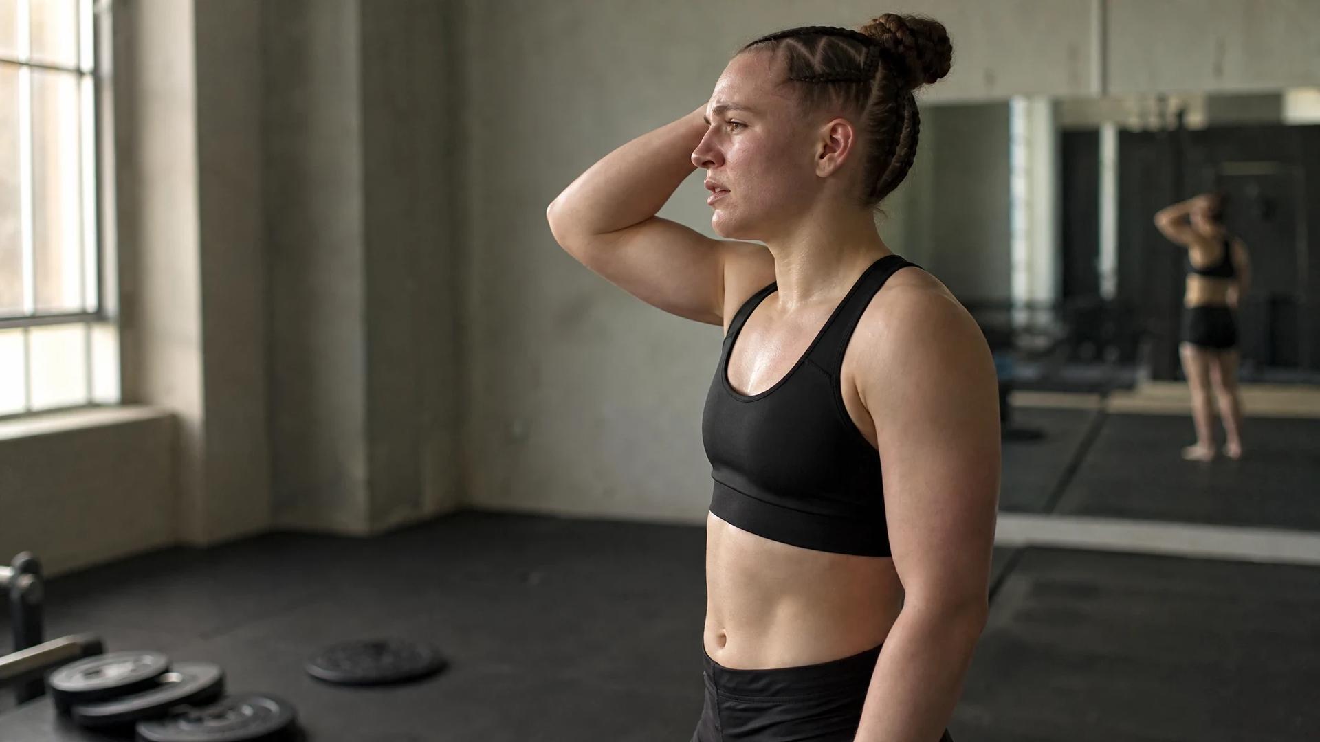 A female fighter in a training area, focused and reflective.