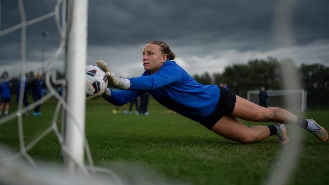 A goalkeeper diving to make a save during a training session on a football pitch.