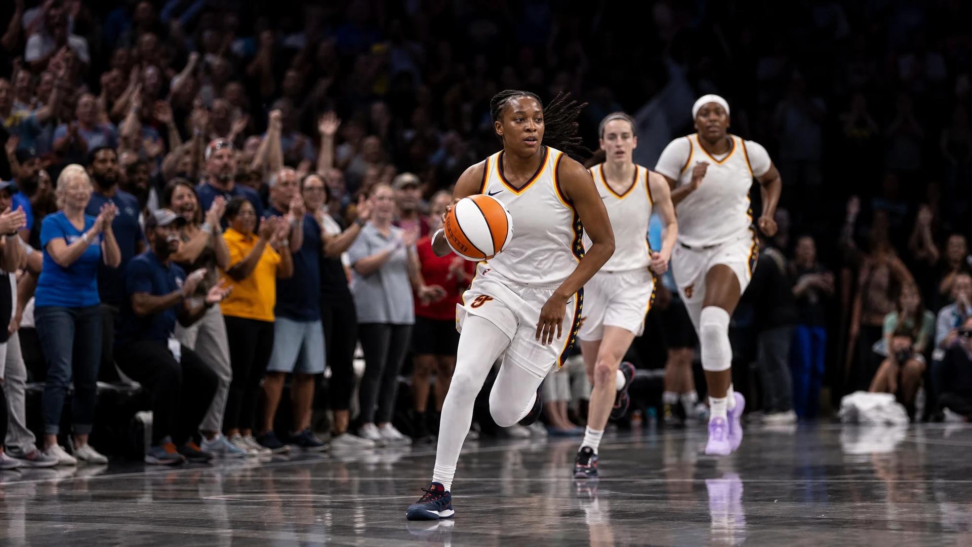 A tense moment as Kelsey Mitchell dribbles the basketball surrounded by enthusiastic fans in Gainbridge Fieldhouse.