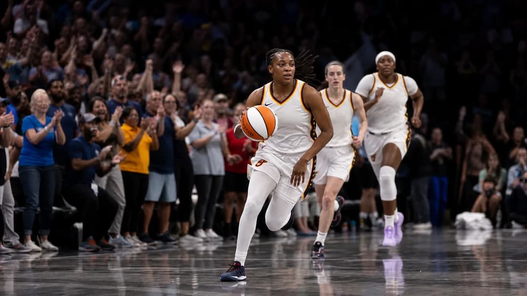 A tense moment as Kelsey Mitchell dribbles the basketball surrounded by enthusiastic fans in Gainbridge Fieldhouse.