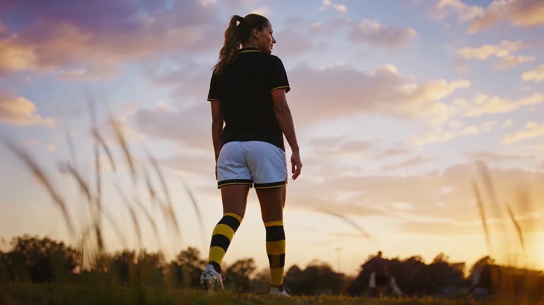 A silhouetted football player stands in a park at twilight, poised before a game.