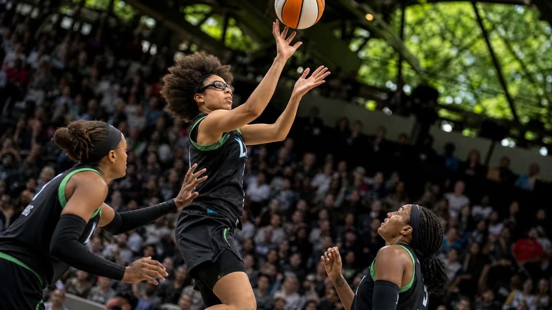 A rookie basketball player leaps and shoots a three-pointer during a game, with teammates nearby and a blurred crowd in the background.