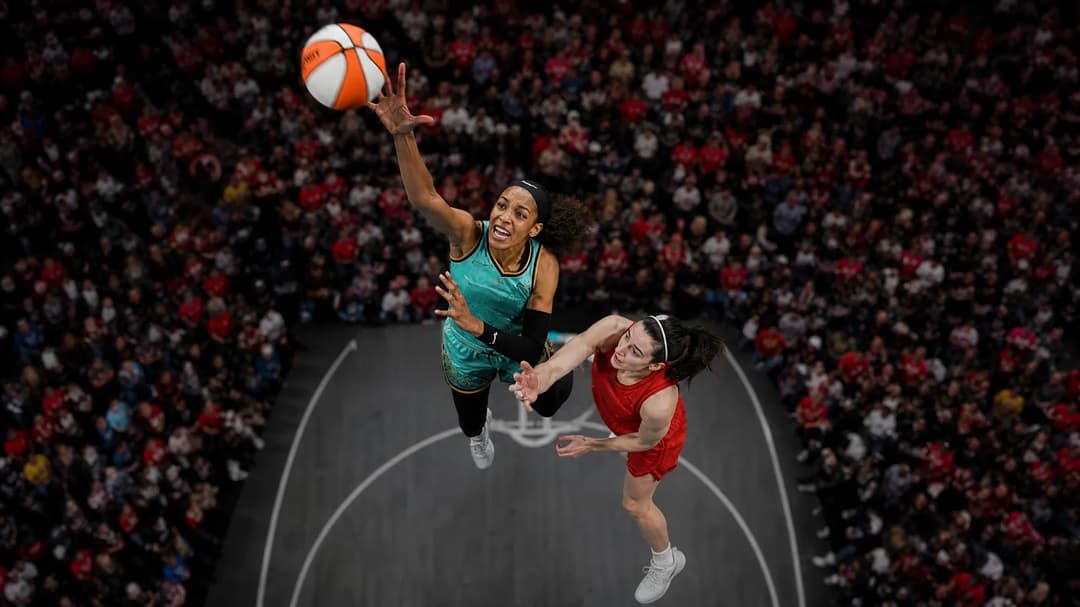 A bird's-eye view of A'ja Wilson and Breanna Stewart competing on a basketball court filled with fans.