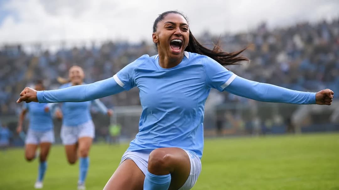 A female football player celebrating on the pitch with arms raised.