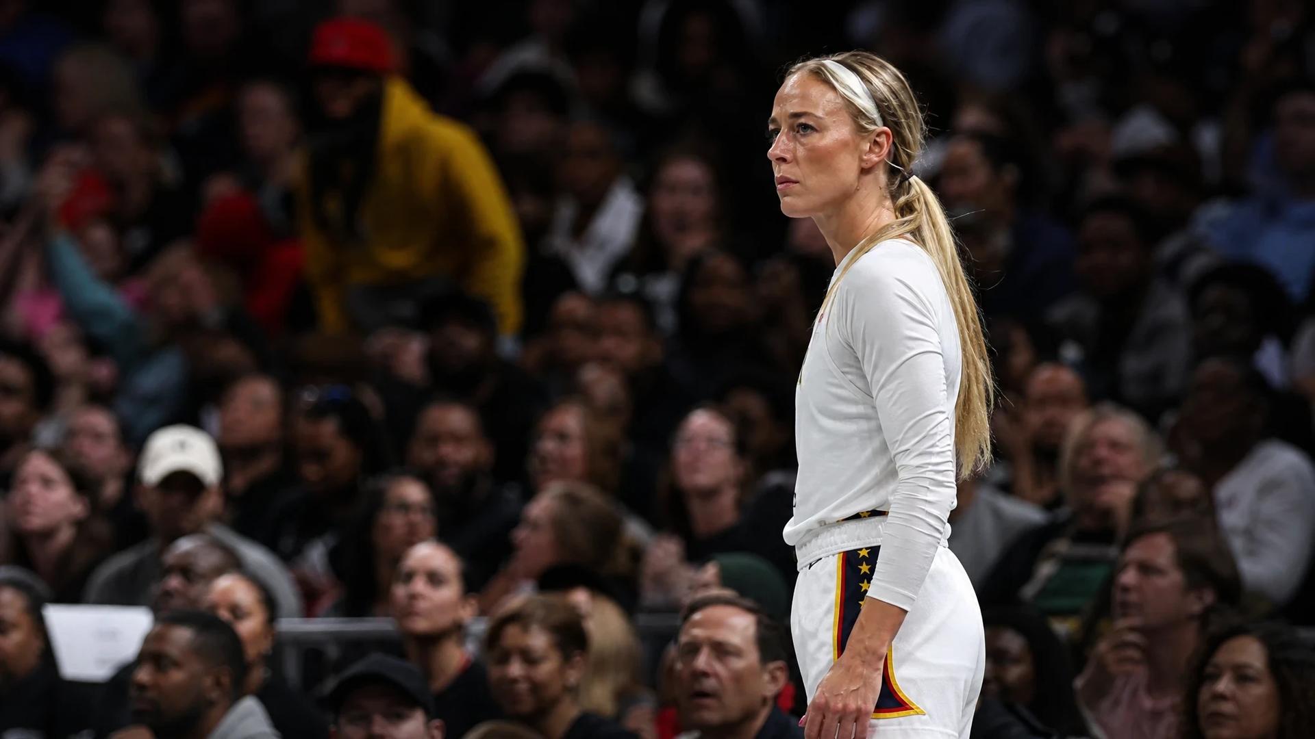 Sophie Cunningham stands at the basketball court, focused on the game as the crowd becomes a blur of excitement behind her.