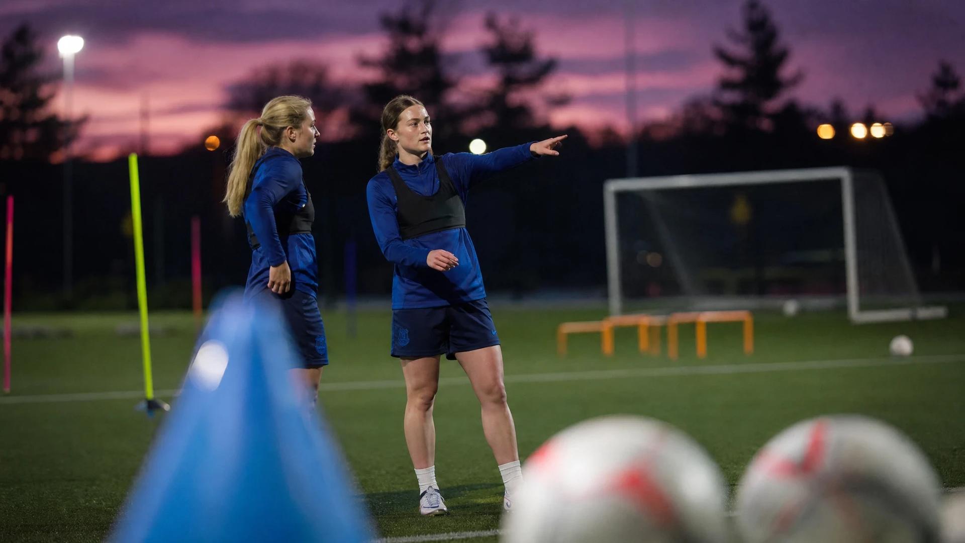 Ruby Mace discussing tactics with a teammate on a football training pitch.