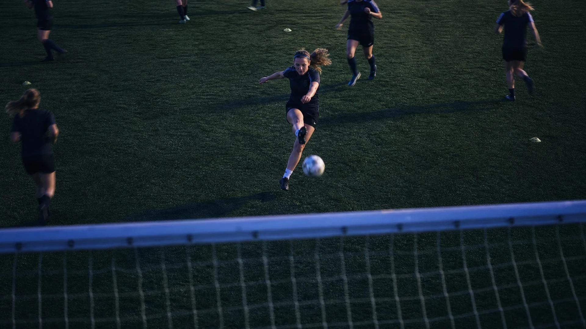 A top-down view of a female football player kicking a ball during training at dusk.