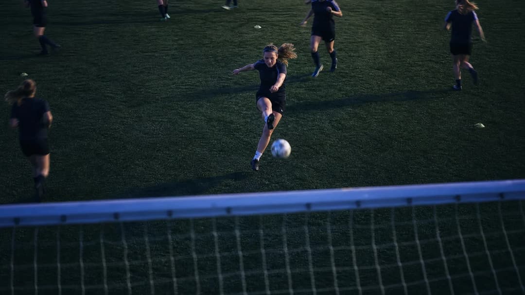 A top-down view of a female football player kicking a ball during training at dusk.