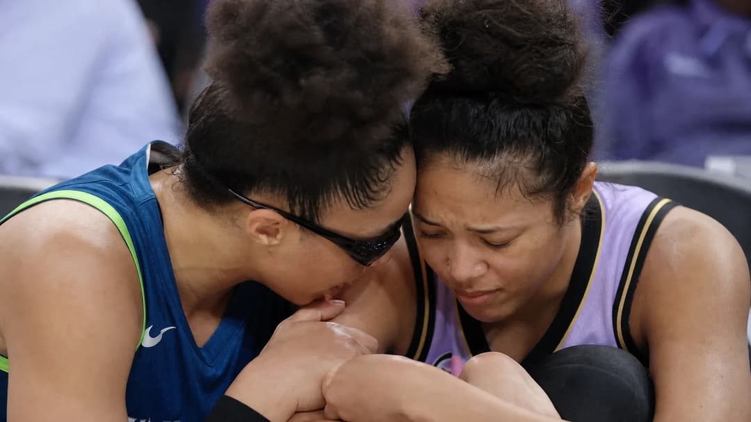 Close-up of two basketball players in a moment of concern and support, one sitting with an injured ankle.