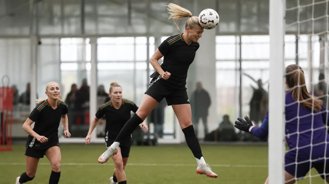 Stina Blackstenius heading a ball during a training match at the Sobha Realty Training Centre with blurred teammates in the background.