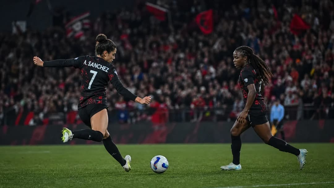 Two female football players from Portland Thorns in action during a match, with a cheering crowd in the background.