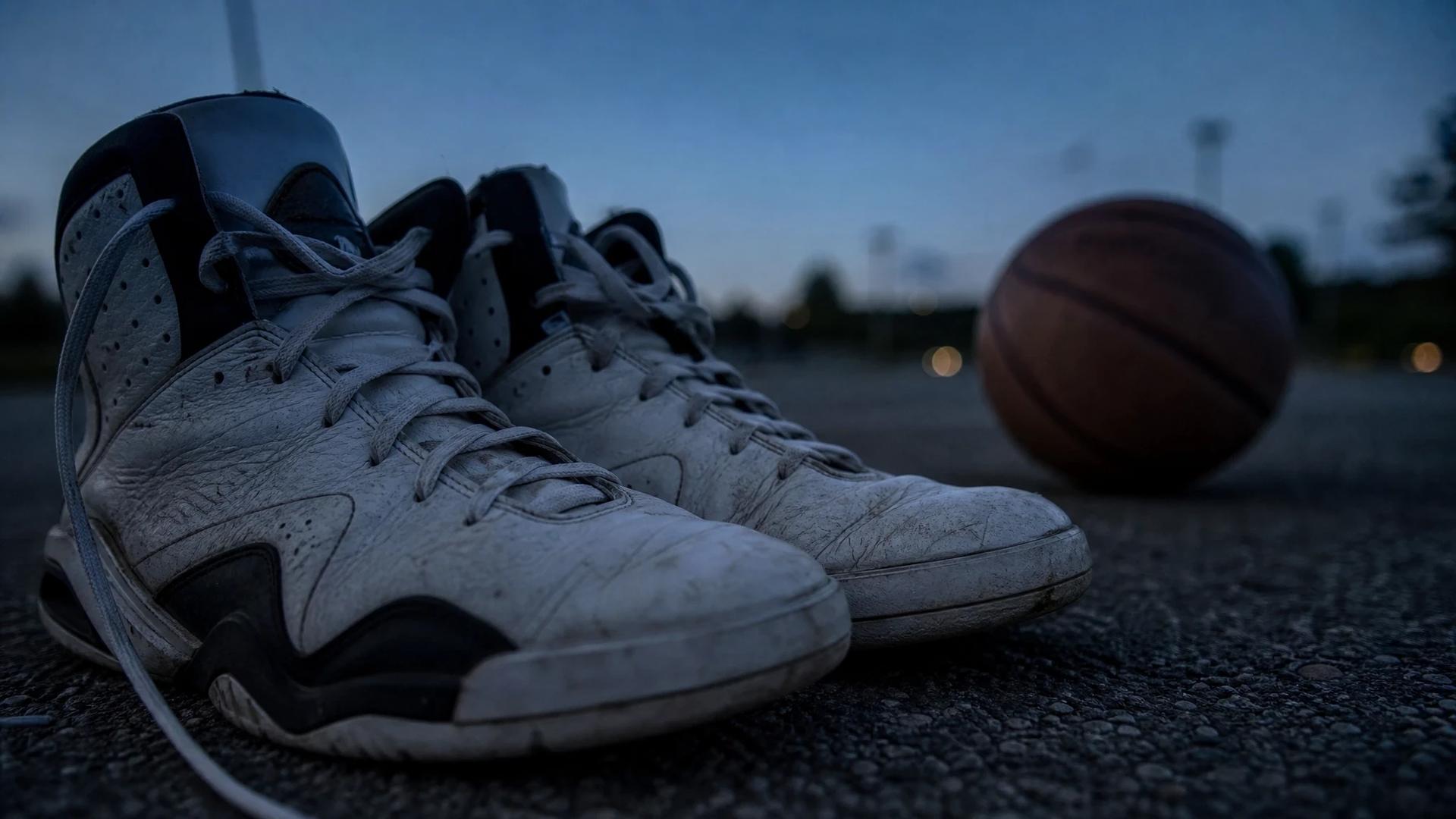 Close-up shot of basketball sneakers and a ball on a deserted court during dusk.