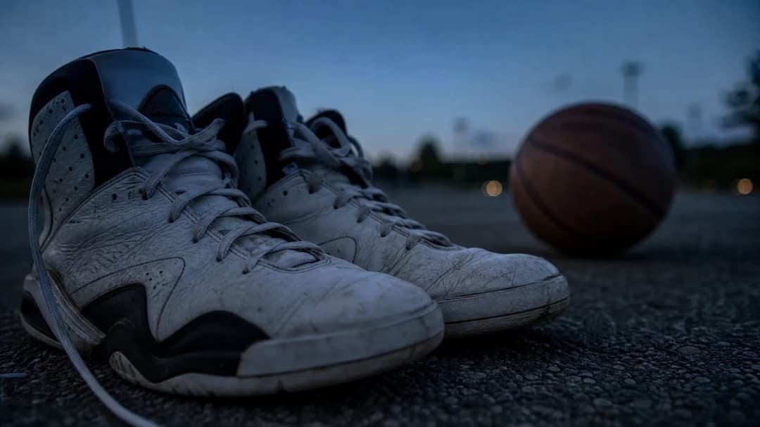 Close-up shot of basketball sneakers and a ball on a deserted court during dusk.