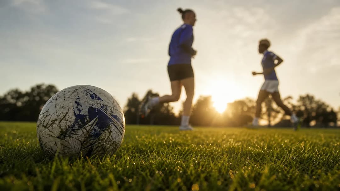 A close-up of a football on grass with players blurred in the background training.